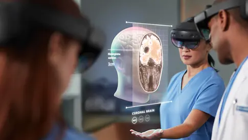 Medical professionals using mixed reality headsets to view and discuss a holographic image of a coronal brain scan.